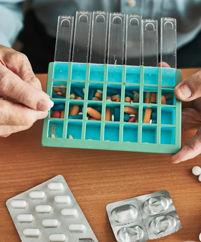 Unabhängig leben mit Demenz - Senior sortiert Tabletten in eine Wochenbox, verschiedene Blisterpackungen mit Medikamenten liegen auf dem Holztisch