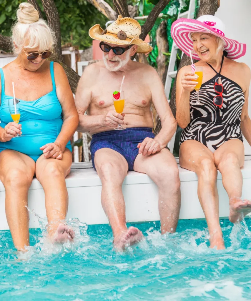 Gruppe von Senioren am Pool sitzend und die Sonne und ausgelassene Stimmung genießen, alle halten bunte Cocktailgläser in der Hand