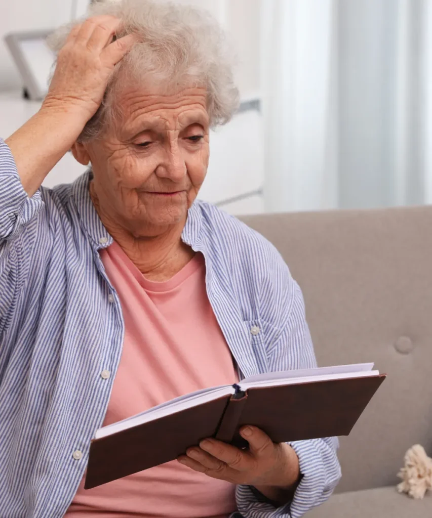 Verwirrte Seniorin mit grauen Haaren beim Lesen eines Buches zeigt mögliche Demenz-Anzeichen