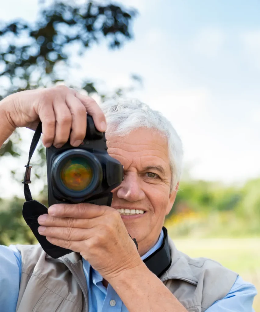Senior fotografiert draußen mit Kamera, Symbol für kreatives Lernen und aktive Freizeitgestaltung im Alter