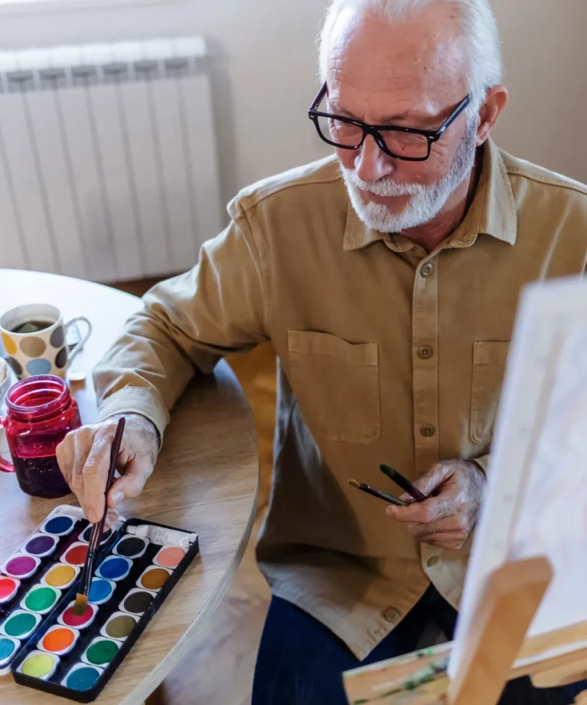 Senior malt mit Aquarellfarben am Tisch, Symbol für kreative Aktivitäten und lebenslanges Lernen bei Senioren