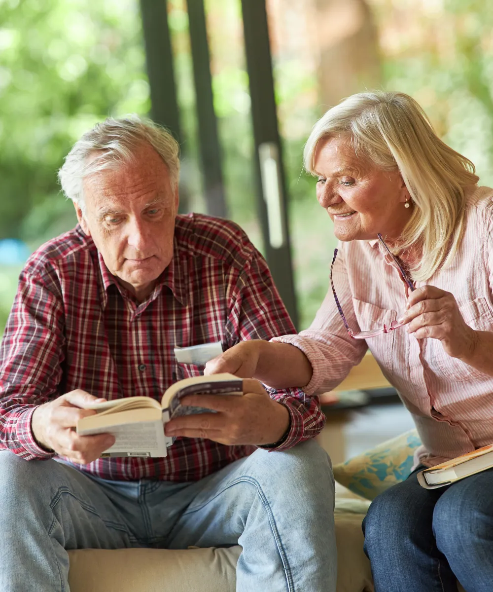 Älteres Ehepaar liest gemeinsam Bücher auf dem Sofa, Symbol für gemeinsames Lernen und geistige Aktivität im Alter