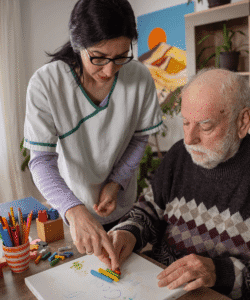 Betreuerin unterstützt älteren Mann bei therapeutischer Aktivität – individuelle Demenz-Betreuung
