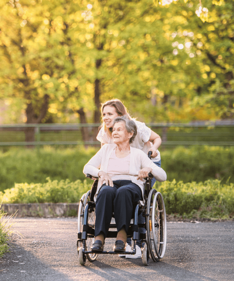 Angehörige schiebt Seniorin im Rollstuhl durch Park – Naturerlebnis als demenzfreundliche Aktivität