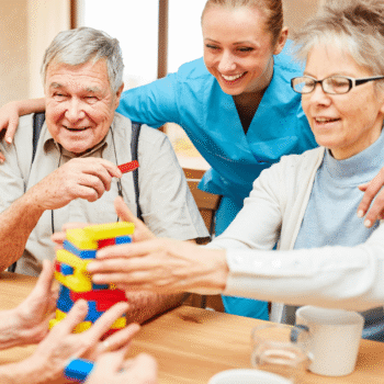 Pflegekraft und Senioren bauen gemeinsam buntes Konstruktionsspiel – kognitive Förderung bei Demenz