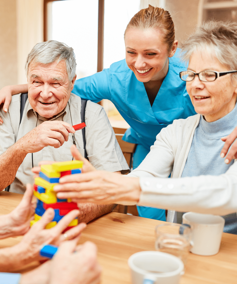 Pflegekraft und Senioren bauen gemeinsam buntes Konstruktionsspiel – kognitive Förderung bei Demenz