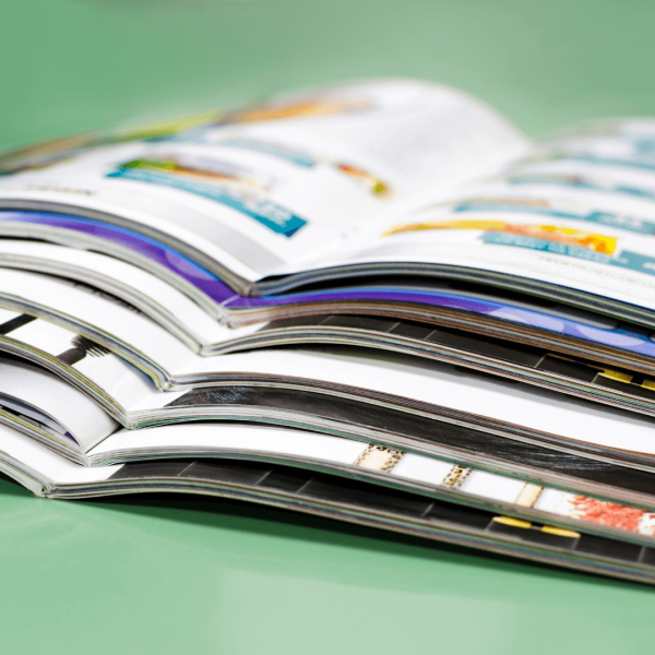 Stapel aufgeschlagener Zeitschriften und Magazine mit bunten Seiten auf grünem Hintergrund, Nahaufnahme der Seitenränder